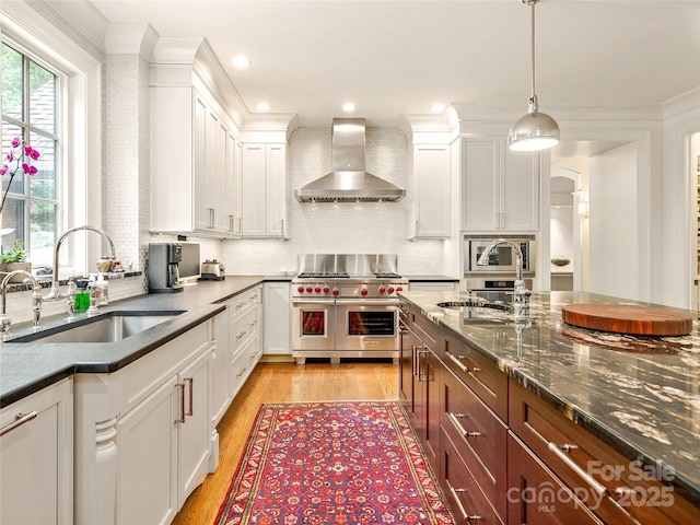 kitchen with sink, wall chimney range hood, range with two ovens, and white cabinetry