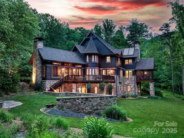 back house at dusk featuring a deck, a lawn, and solar panels