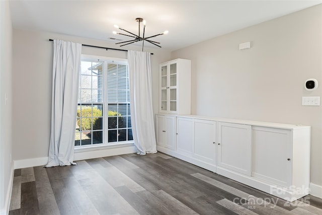 unfurnished dining area with a chandelier, baseboards, visible vents, and wood finished floors