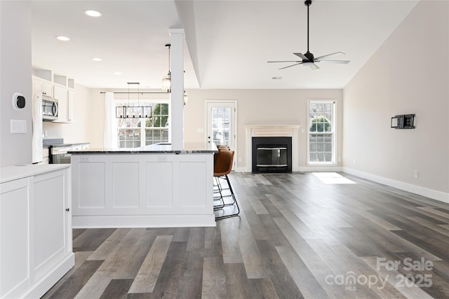 kitchen featuring dark wood-type flooring, stainless steel microwave, open floor plan, a glass covered fireplace, and white cabinetry