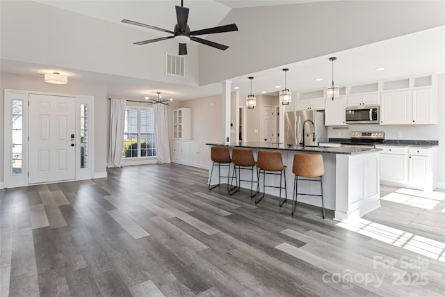 kitchen with an island with sink, a sink, dark countertops, appliances with stainless steel finishes, and a breakfast bar area