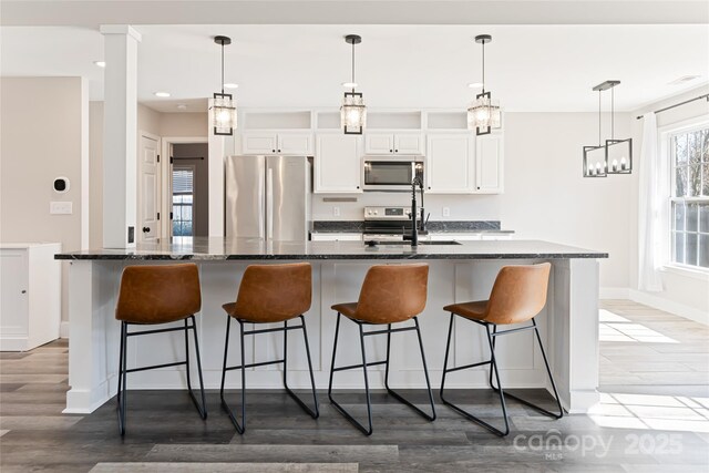 kitchen with a kitchen bar, stainless steel appliances, white cabinets, light wood finished floors, and a large island with sink