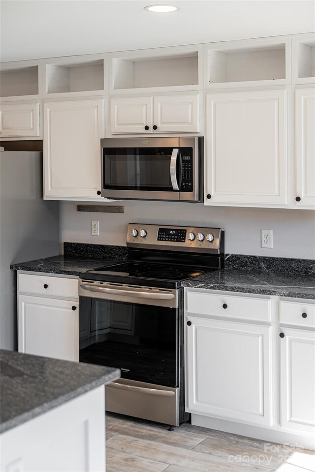 kitchen featuring dark stone counters, white cabinets, light wood-style flooring, and appliances with stainless steel finishes