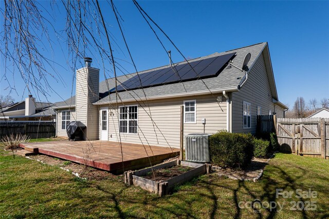 rear view of house with central AC, a fenced backyard, a yard, a vegetable garden, and solar panels