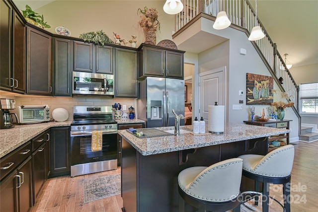 kitchen featuring light stone counters, stainless steel appliances, light hardwood / wood-style floors, a breakfast bar area, and an island with sink