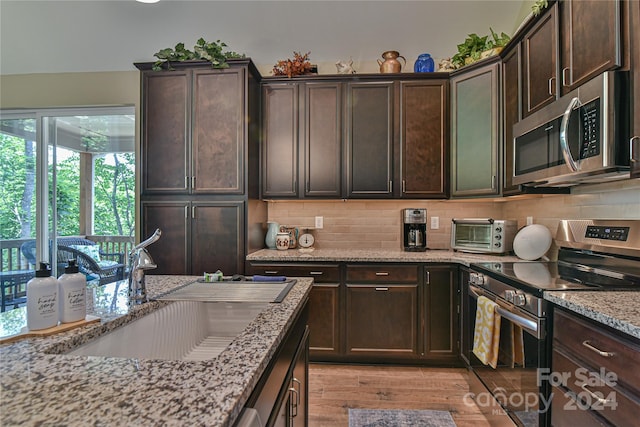 kitchen featuring dark brown cabinetry, light stone countertops, light hardwood / wood-style flooring, and stainless steel appliances