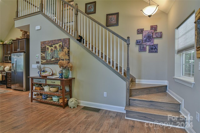 stairs with hardwood / wood-style floors and high vaulted ceiling