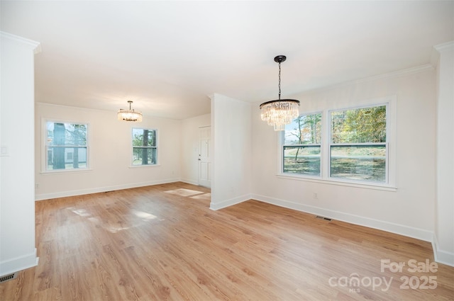 empty room featuring a healthy amount of sunlight, light wood-type flooring, ornamental molding, and an inviting chandelier