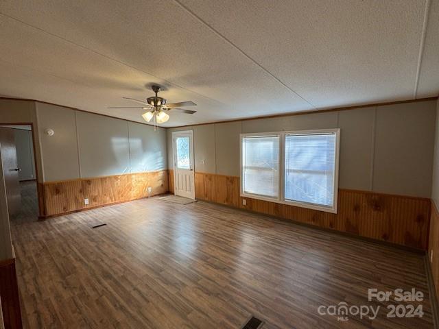 spare room featuring ceiling fan, wooden walls, dark wood-type flooring, and a textured ceiling