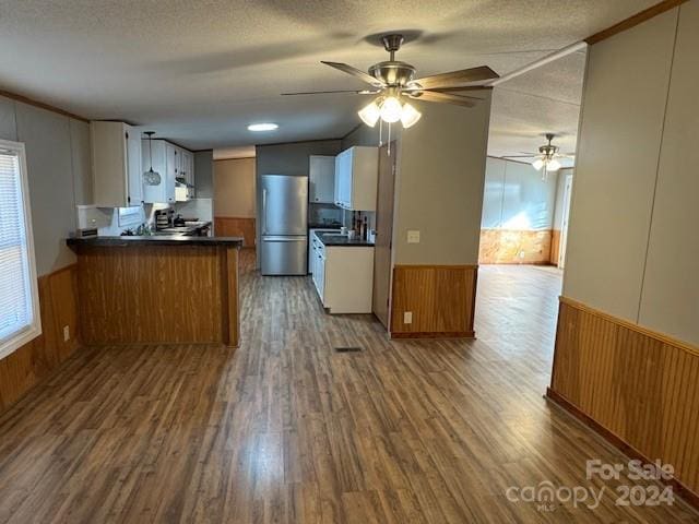 kitchen with kitchen peninsula, stainless steel fridge, a textured ceiling, white cabinets, and hardwood / wood-style floors