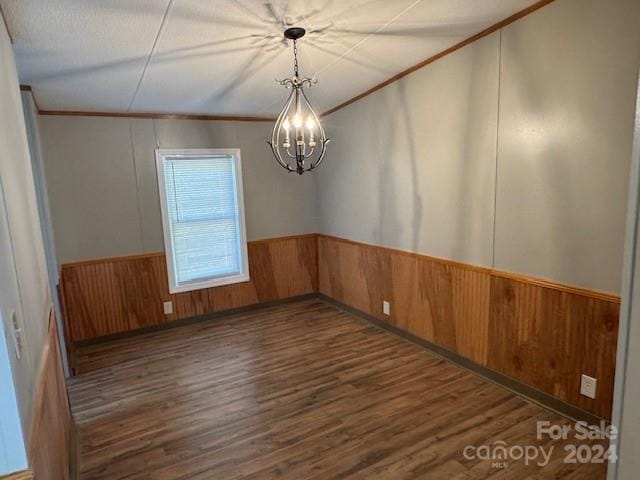 unfurnished room with wooden walls, dark hardwood / wood-style floors, crown molding, and a notable chandelier