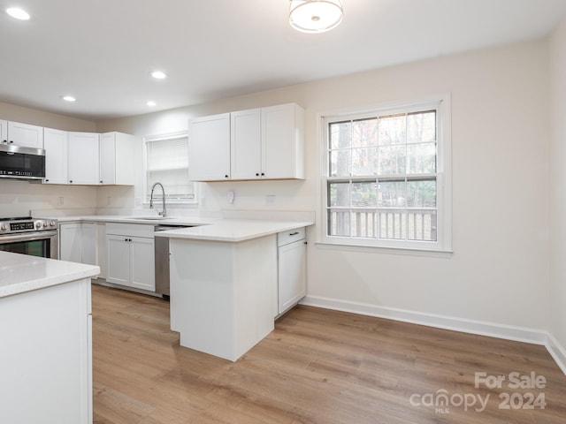 kitchen with sink, light hardwood / wood-style flooring, kitchen peninsula, white cabinets, and appliances with stainless steel finishes