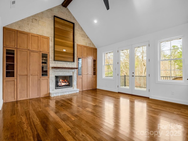 unfurnished living room featuring french doors, a stone fireplace, high vaulted ceiling, hardwood / wood-style flooring, and beamed ceiling