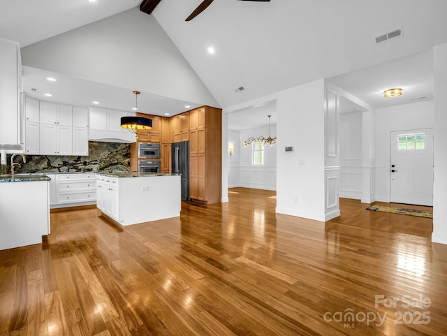 kitchen with white cabinetry, hanging light fixtures, dark stone countertops, a center island, and light wood-type flooring