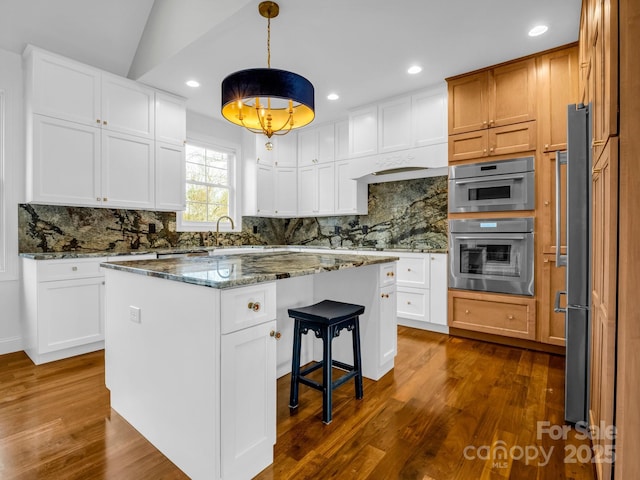 kitchen featuring pendant lighting, dark stone countertops, backsplash, white cabinets, and a kitchen island