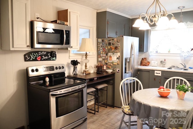 kitchen featuring light wood-type flooring, ornamental molding, stainless steel appliances, sink, and decorative light fixtures