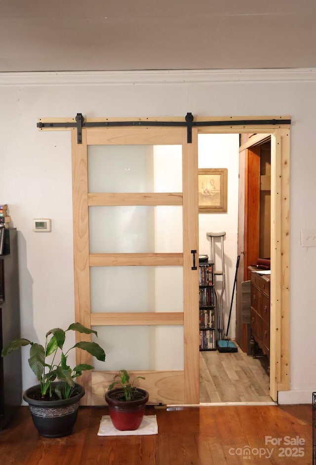 interior space with a barn door, crown molding, and hardwood / wood-style floors