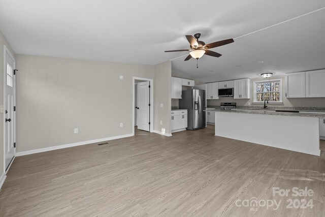 kitchen with white cabinets, light stone counters, appliances with stainless steel finishes, and light hardwood / wood-style flooring