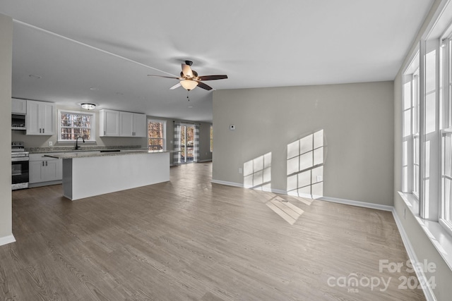 unfurnished living room with ceiling fan, hardwood / wood-style floors, vaulted ceiling, and sink