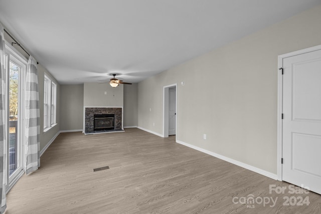 unfurnished living room featuring a stone fireplace, ceiling fan, and light hardwood / wood-style floors