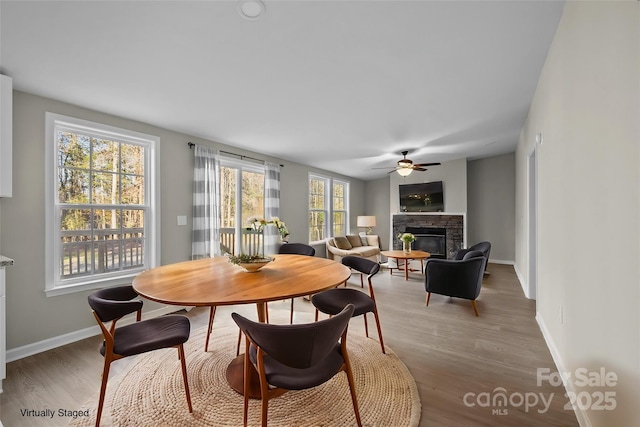 dining space featuring hardwood / wood-style floors, a stone fireplace, and ceiling fan