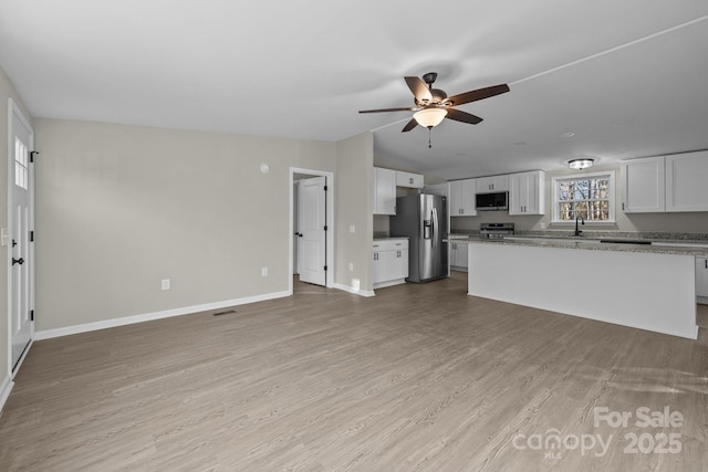 unfurnished living room featuring white cabinetry, vaulted ceiling, light stone counters, and light wood-type flooring