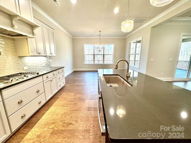 kitchen featuring sink, decorative light fixtures, stainless steel gas stovetop, hardwood / wood-style flooring, and ornamental molding