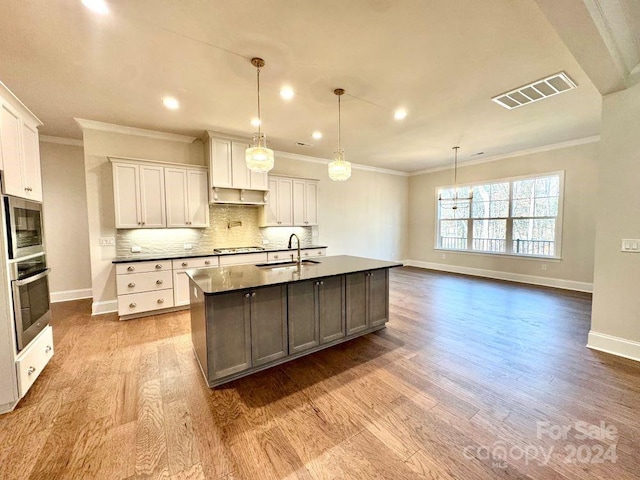 kitchen with white cabinets, stainless steel appliances, light hardwood / wood-style flooring, and an island with sink