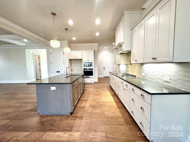 kitchen with pendant lighting, a large island with sink, white cabinets, sink, and light wood-type flooring