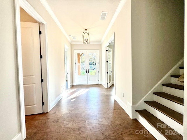 entryway with french doors, an inviting chandelier, ornamental molding, and dark wood-type flooring