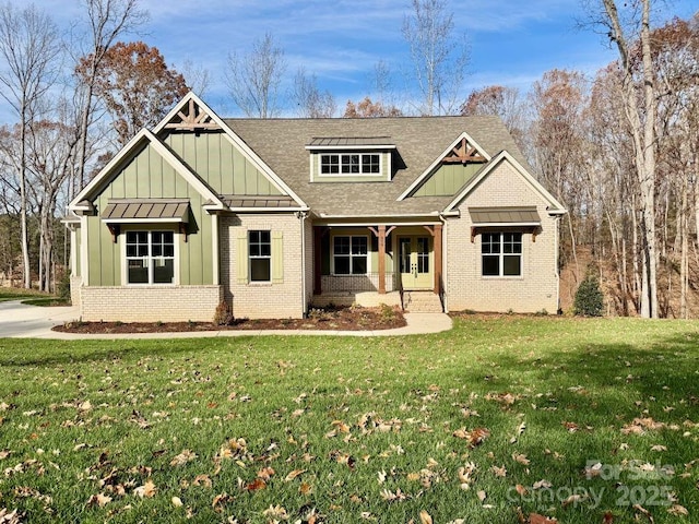 view of front of property with board and batten siding, brick siding, a shingled roof, and a front lawn