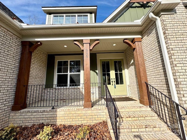 view of exterior entry featuring board and batten siding, french doors, brick siding, and a porch