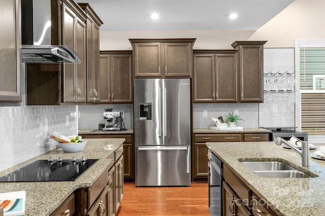 kitchen featuring wall chimney exhaust hood, sink, light stone counters, and stainless steel appliances