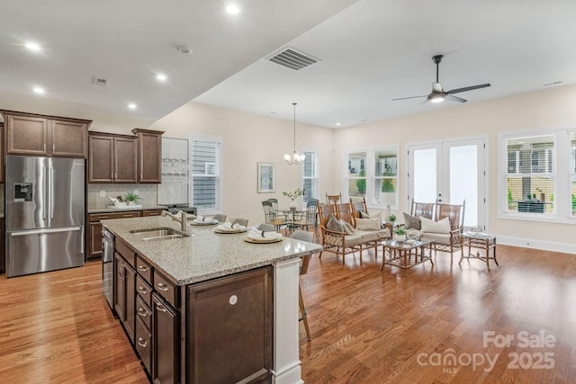 kitchen featuring sink, light stone counters, backsplash, a kitchen island with sink, and appliances with stainless steel finishes