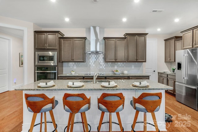 kitchen featuring stainless steel appliances, a center island with sink, wall chimney exhaust hood, and sink