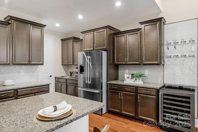 kitchen featuring decorative backsplash, stainless steel refrigerator with ice dispenser, light wood-type flooring, light stone countertops, and wine cooler