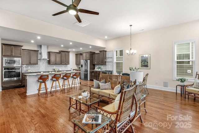 living room with ceiling fan with notable chandelier and light wood-type flooring