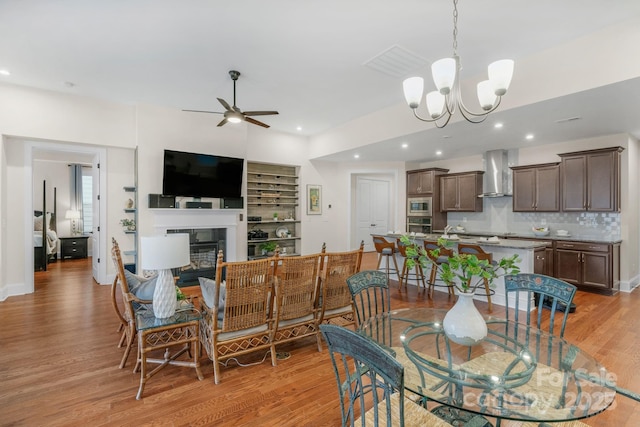 dining space with ceiling fan with notable chandelier and light hardwood / wood-style floors