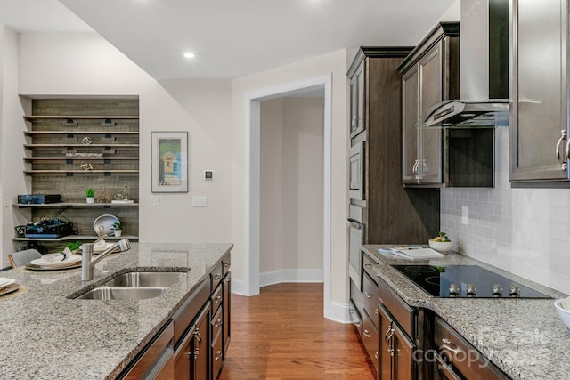 kitchen featuring sink, wall chimney exhaust hood, light stone counters, backsplash, and appliances with stainless steel finishes