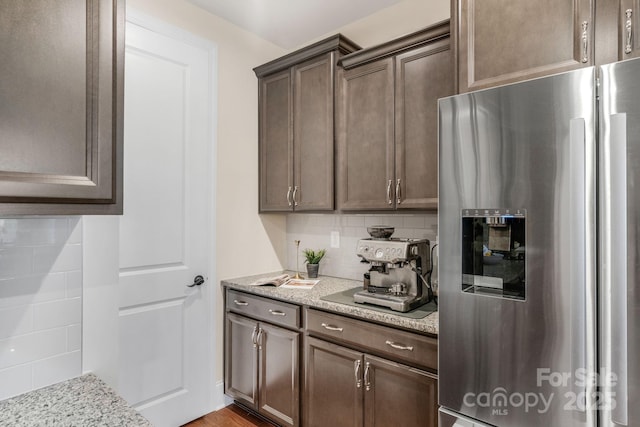 kitchen with dark brown cabinets, light stone counters, stainless steel fridge with ice dispenser, and backsplash