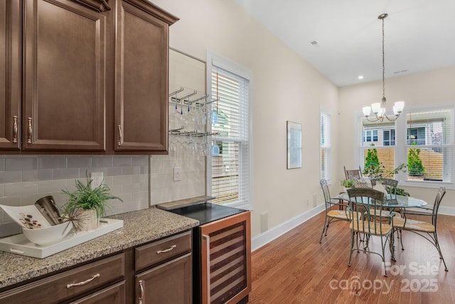 kitchen with beverage cooler, an inviting chandelier, light stone counters, backsplash, and light hardwood / wood-style floors