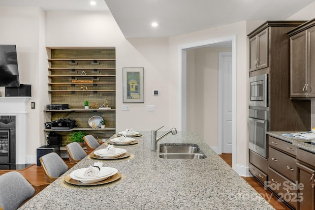 kitchen featuring sink, stainless steel microwave, a kitchen breakfast bar, light stone counters, and a fireplace