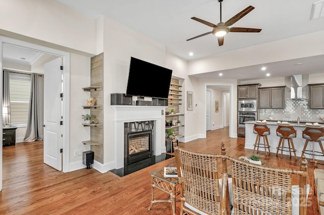 living room featuring light wood-type flooring, ceiling fan, and sink