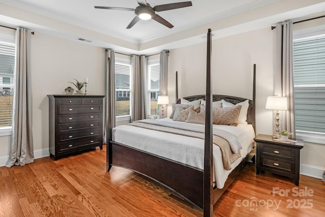 bedroom with hardwood / wood-style floors, a tray ceiling, ceiling fan, and ornamental molding