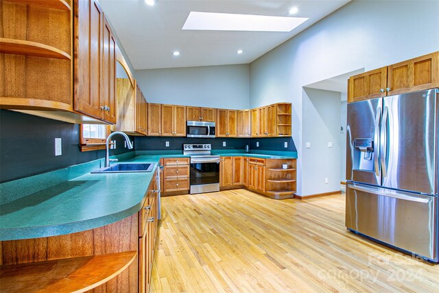 kitchen featuring appliances with stainless steel finishes, light wood-type flooring, a skylight, sink, and high vaulted ceiling