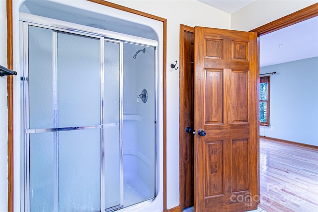 full bath with a shower stall, wood finished floors, and baseboards