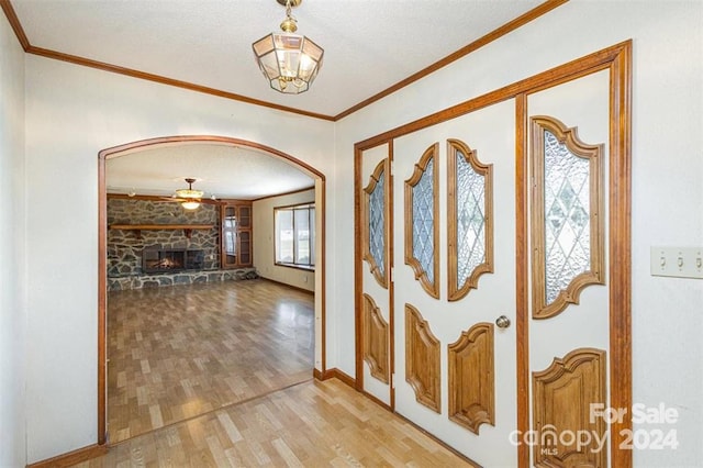 entryway featuring ceiling fan, a stone fireplace, crown molding, wood-type flooring, and a textured ceiling