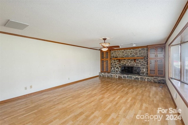 unfurnished living room featuring wood-type flooring, a textured ceiling, a stone fireplace, and ornamental molding