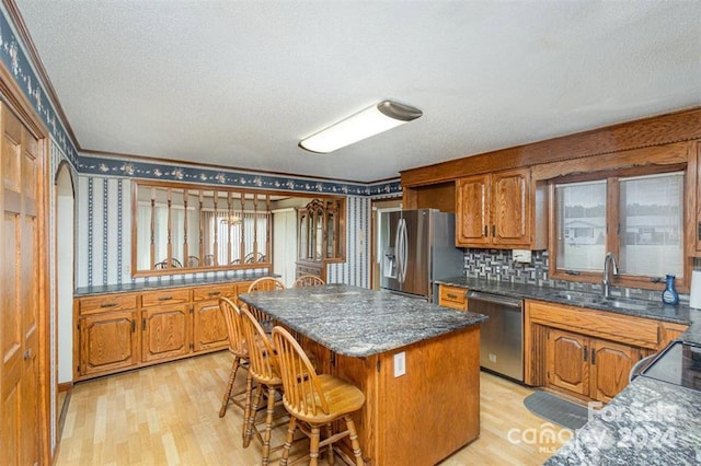 kitchen with a kitchen bar, stainless steel appliances, sink, light hardwood / wood-style flooring, and a center island