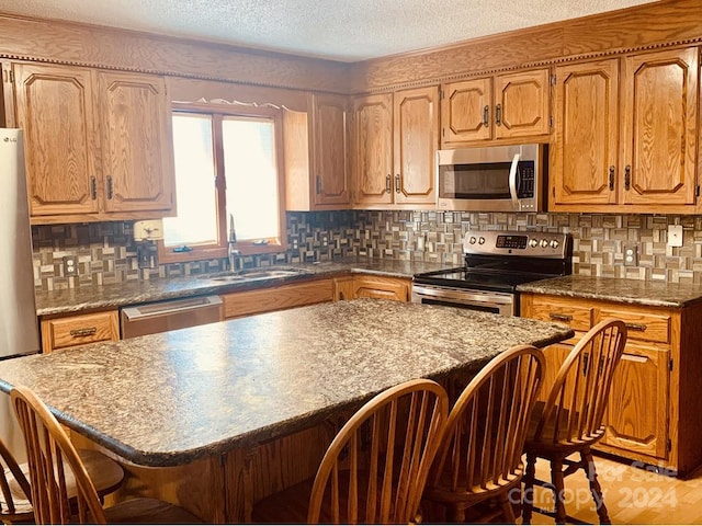 kitchen with backsplash, a breakfast bar area, a textured ceiling, and appliances with stainless steel finishes